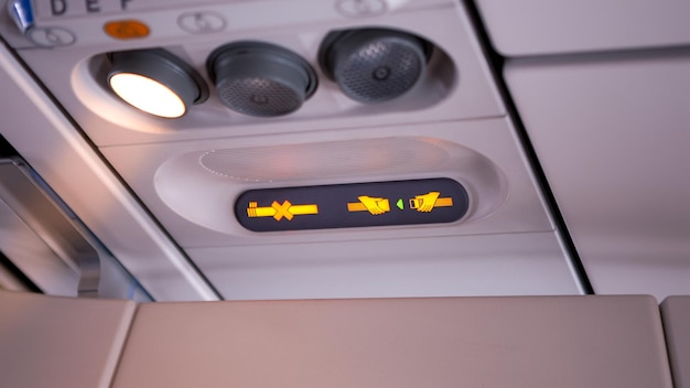 Primer plano de un panel de luz de seguridad del avión que muestra el cinturón de seguridad y la prohibición de fumar