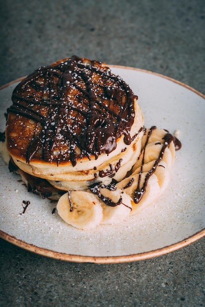 Primer plano de panqueques con chocolate y plátanos servidos en un plato blanco