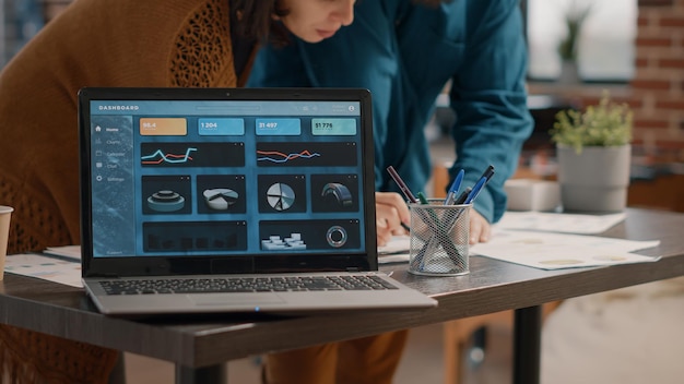 Primer plano de la pantalla del portátil con gráficos de tasa de datos en el escritorio mientras los colegas trabajan en un proyecto empresarial. Pantalla de computadora con información gráfica y análisis para diseñar la estrategia de trabajo