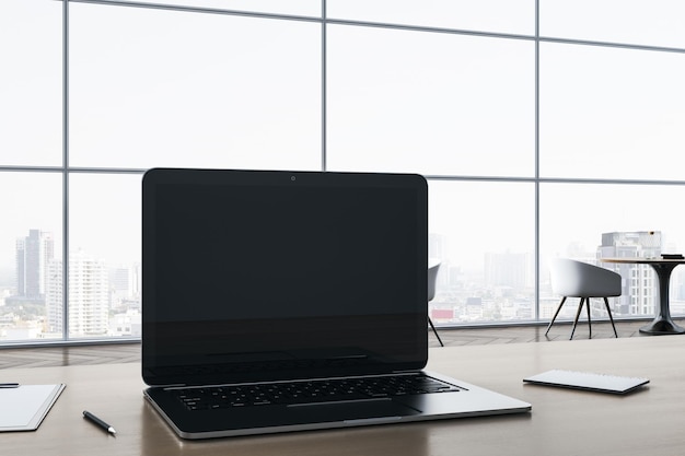 Primer plano de la pantalla vacía del portátil en el escritorio de la oficina de madera con suministros en la ventana panorámica y el telón de fondo de la vista de la ciudad Mock up 3D Rendering