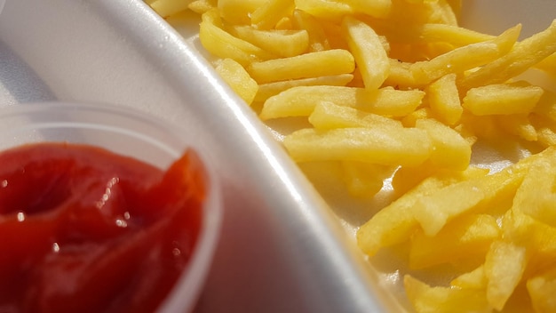 Un primer plano de papas fritas de color amarillo anaranjado dorado con salsa de tomate servido en un recipiente de espuma. Comida rápida para llevar. Alimentos frescos no deseados.