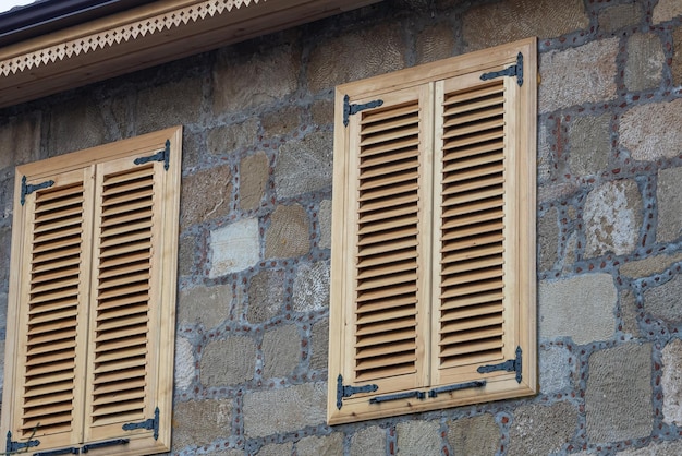 Primer plano de la pared de una casa de piedra con ventanas y persianas de madera Vieja arquitectura europea