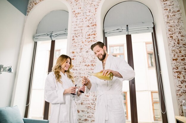 Primer plano de una pareja bebiendo champán en la habitación del hotel. Hombre guapo vierte champán en copas