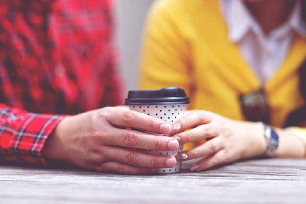 Foto primer plano de una pareja de manos sosteniendo una taza desechable en la mesa