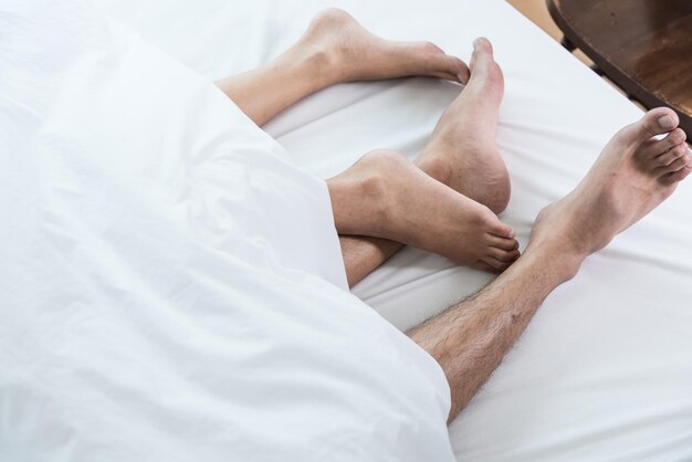 Primer plano de una pareja de pies en la cama, pies de pareja en una cama cómoda bajo una sábana blanca