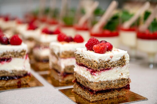 Primer plano de pasteles con frutas frescas y bayas dispuestas en fila en una mesa de fiesta