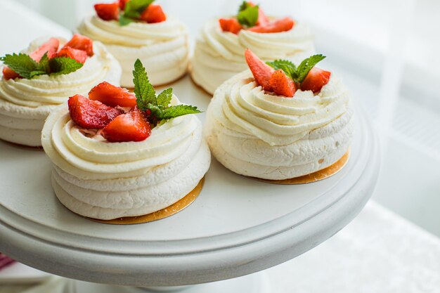 Primer plano de pasteles de merengue pavlova con crema batida de fresas y menta ubicado en el soporte blanco