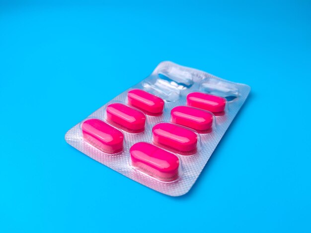 Primer plano de pastillas de antibióticos rosadas en envases grises aislados sobre un fondo azul