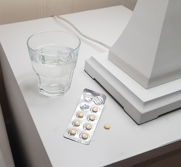 Primer plano de pastillas para dormir y un vaso de agua preparado para un sueño tranquilo y profundo en la mesita de noche del dormitorio, el concepto de salud y enfermedad.