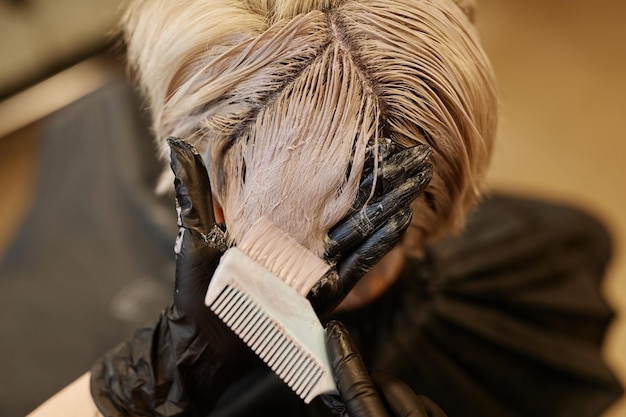 Foto primer plano de un peluquero aplicando blanqueador o tinte a las hebras de cabello en un salón de belleza