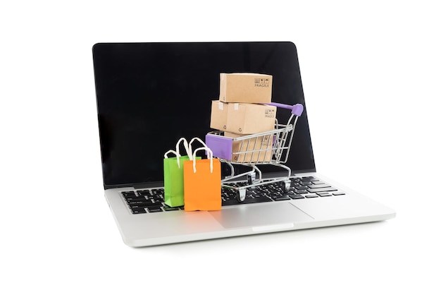Primer plano de pequeñas bolsas de compras y carrito en la computadora portátil contra un fondo blanco