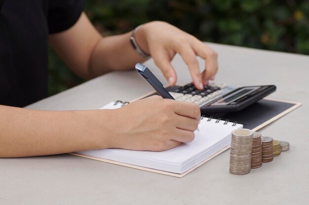 Foto primer plano de una persona escribiendo en un libro mientras usa una calculadora en la mesa