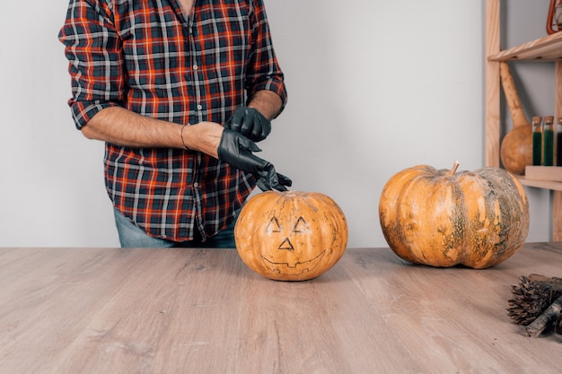Foto un primer plano de una persona con guantes de látex y preparándose para tallar una calabaza para halloween