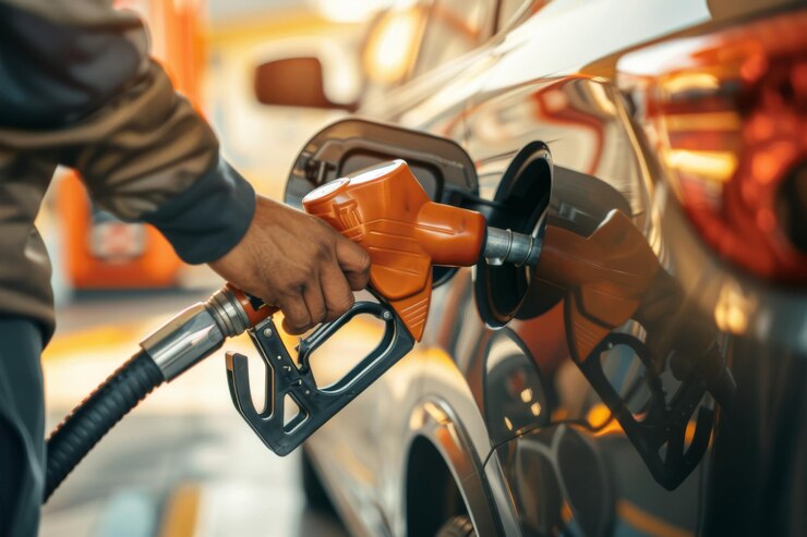Primer plano de una persona llenando de combustible un coche amarillo en una gasolinera centrándose en la boquilla de combustible y el vehículo