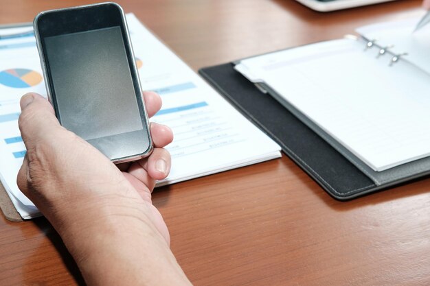 Foto primer plano de una persona de negocios usando el teléfono mientras trabaja sobre un gráfico en la mesa