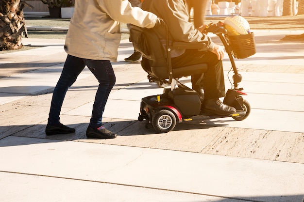 Foto primer plano de una persona que empuja al hombre sentado sobre un scooter de movilidad en la calle