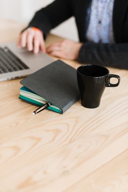 Primer plano de una persona que trabaja en casa en una computadora portátil sentada en un escritorio. El diario está sobre la mesa. Trabaja en el escritorio.