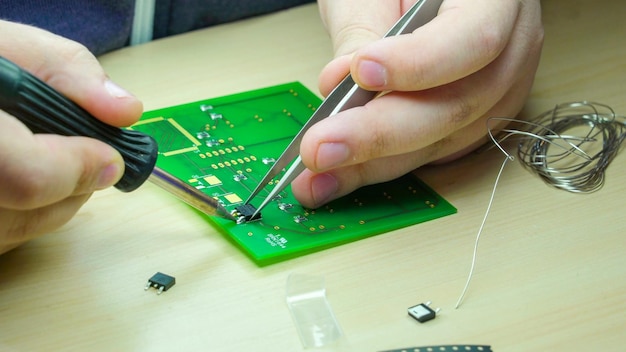 Primer plano de una persona reparando una placa de circuitos en la mesa