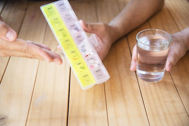 Foto primer plano de una persona con un vaso de agua en la mano con una caja de pastillas en la mesa