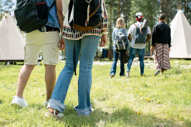 Primer plano de personas con carteras de pie sobre el césped y eligiendo carpas en el campamento del festival