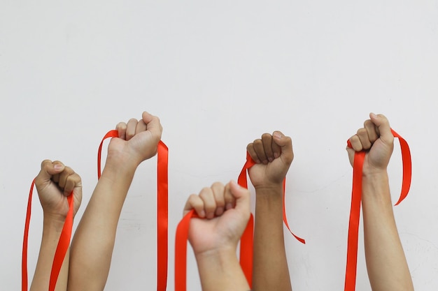 Foto primer plano de personas levantan sus manos con cintas rojas para concienciar sobre el sida