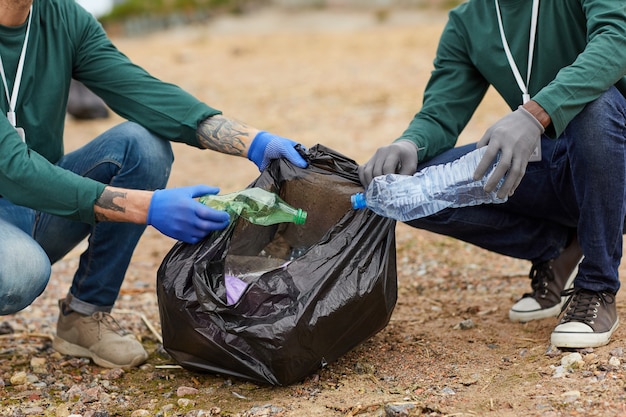 Primer plano de personas poniendo la basura en las grandes bolsas negras al aire libre