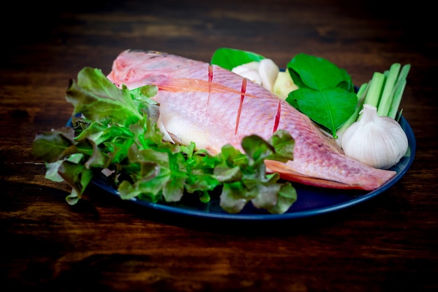 Primer plano de un pescado fresco y verduras en platos de cerámica preparados para cocinar