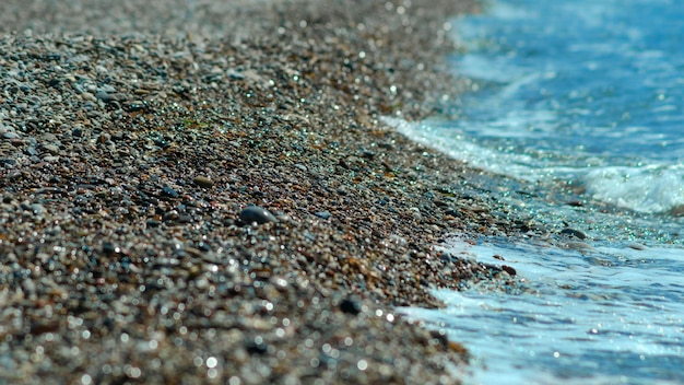 Primer plano de piedras de playa y agua de mar que brilla en la luz del sol