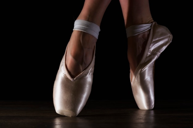 Primer plano de las piernas de la bailarina clásica en pointes en el piso negro