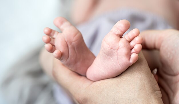 Primer plano de las piernas del bebé recién nacido en manos de mamá sobre fondo borroso.