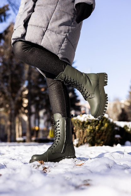 Primer plano de piernas femeninas en botas verdes de pie en la nieve Zapatos de invierno de cuero de mujer