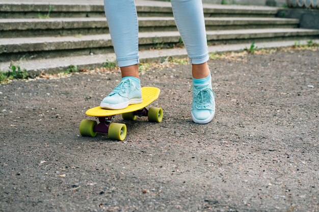 Primer plano de las piernas femeninas en jeans y zapatillas de deporte montando un monopatín en el parque