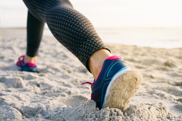 Foto primer plano de las piernas femeninas en medias y zapatillas de deporte durante el ejercicio de la mañana en la playa