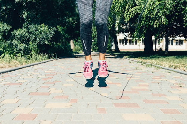 Primer plano de piernas femeninas en zapatillas de deporte saltar la cuerda en verano al aire libre, ángulo bajo