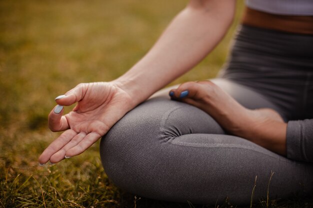 Primer plano de las piernas de una mujer sentada en posición de loto y meditando y con los dedos en Gyan mudra al atardecer en tsummer en el bosque.