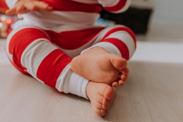 Primer plano de los pies descalzos de un bebé en pijama de rayas de Navidad sentado en un piso de madera