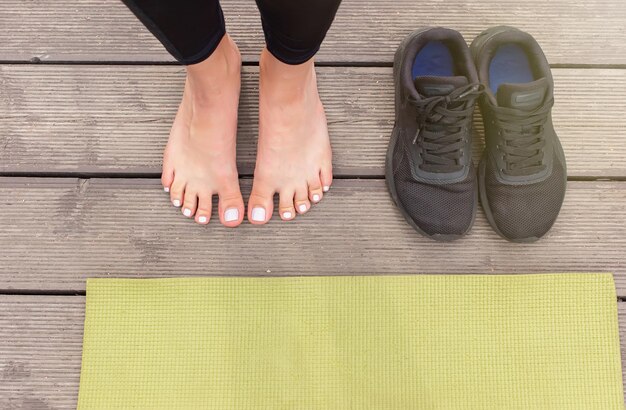 Foto primer plano de pies descalzos sobre un suelo de madera cerca de una alfombra deportiva verde hay zapatillas negras cerca en verano cerca de un estanque en el parque vista superior espacio de copia