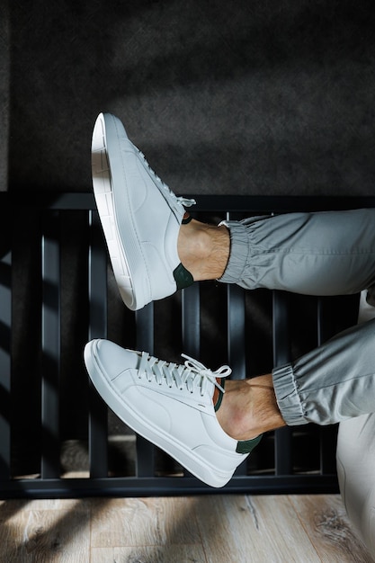 Hombre joven moderno de moda en jeans con estilo en unas zapatillas blancas  de temporada de cuero de moda se encuentra en un estacionamiento en la  ciudad. primer plano de las piernas