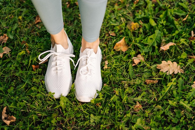 Primer plano de pies de mujer en zapatillas blancas de pie y poses en su lugar sobre hierba verde