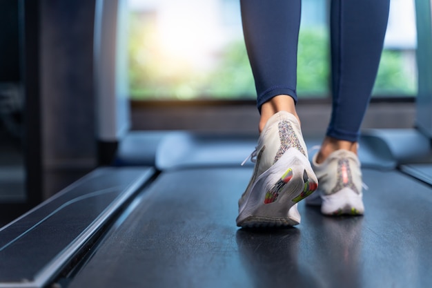 Foto primer plano los pies de las mujeres se ejecutan en una cinta de correr en el gimnasio. las mujeres se estiran, se calientan antes de cardio en el deporte y el concepto saludable.