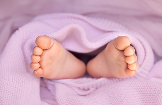 Foto primer plano de los pies de la niña envueltos en una manta rosa pastel