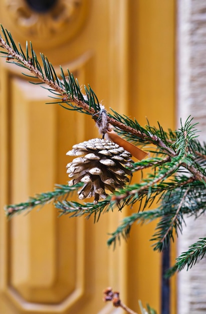 Primer plano de piña aferrada al árbol de Navidad frente a la puerta amarilla vintage Navidad