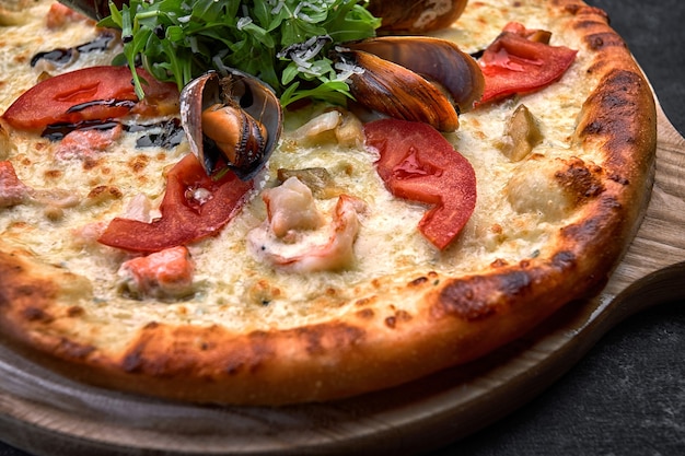 Primer plano de una pizza de mariscos en la plancha de madera sobre mostrador de piedra oscura