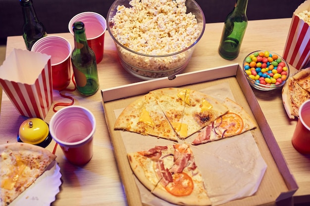 Primer plano de pizza, palomitas de maíz y bebidas alcohólicas en la mesa de la fiesta