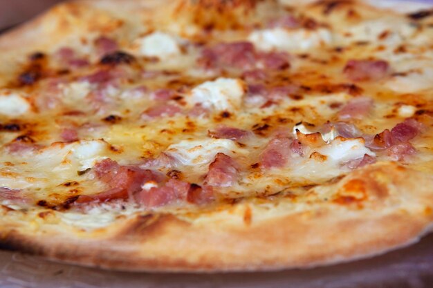Un primer plano de una pizza con queso con jamón y crema