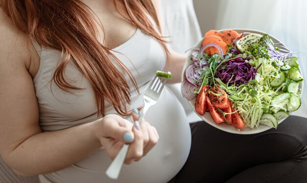 Primer plano de un plato con una brillante ensalada de verduras frescas en manos de una mujer embarazada.