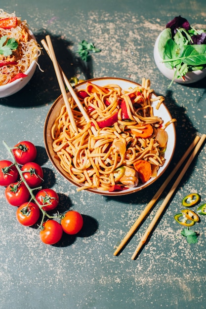 Primer plano de un plato de fideos chinos con carne y verduras en platos y palillos chinos en verde