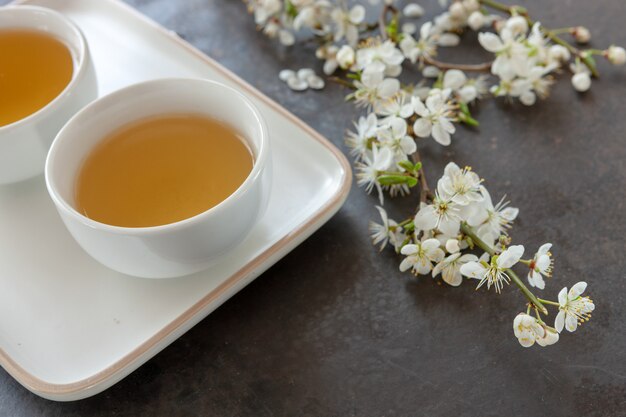 Primer plano de la porcelana de té asiático blanco conjunto con té verde japón con ramas en flor de cerezo