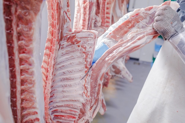 Primer plano del procesamiento de carne en la industria alimentaria un trabajador corta carne de cerdo cruda el concepto de productos cárnicos