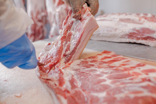 Primer plano del procesamiento de carne en la industria alimentaria un trabajador corta carne de cerdo cruda el concepto de productos cárnicos